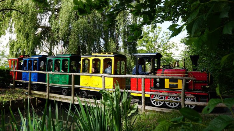 Wattman Maxi Express travelling through a tree-lined city park with families enjoying a scenic community ride